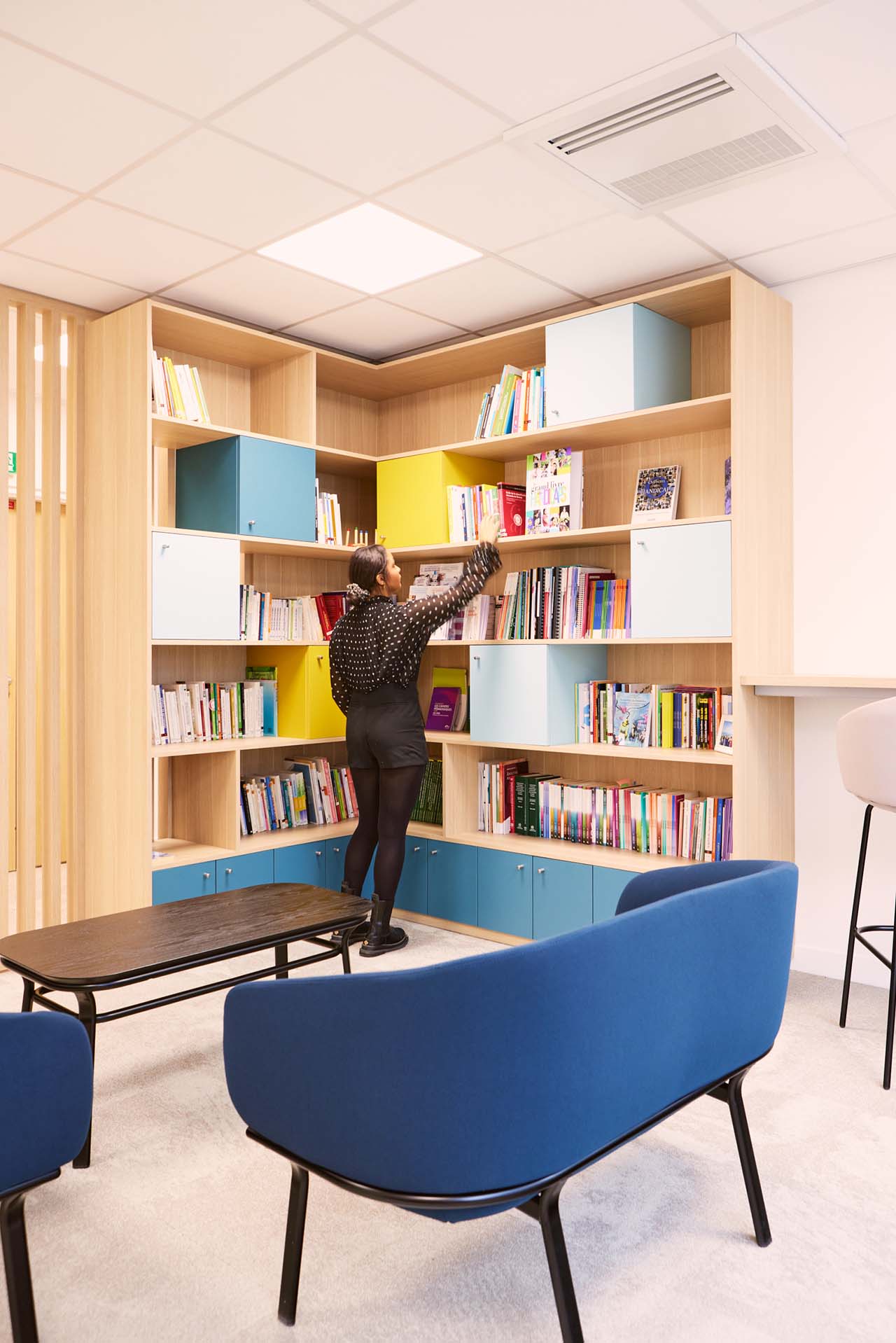 Employée qui prend le livre d'une bibliothèque en bois faite sur mesure
